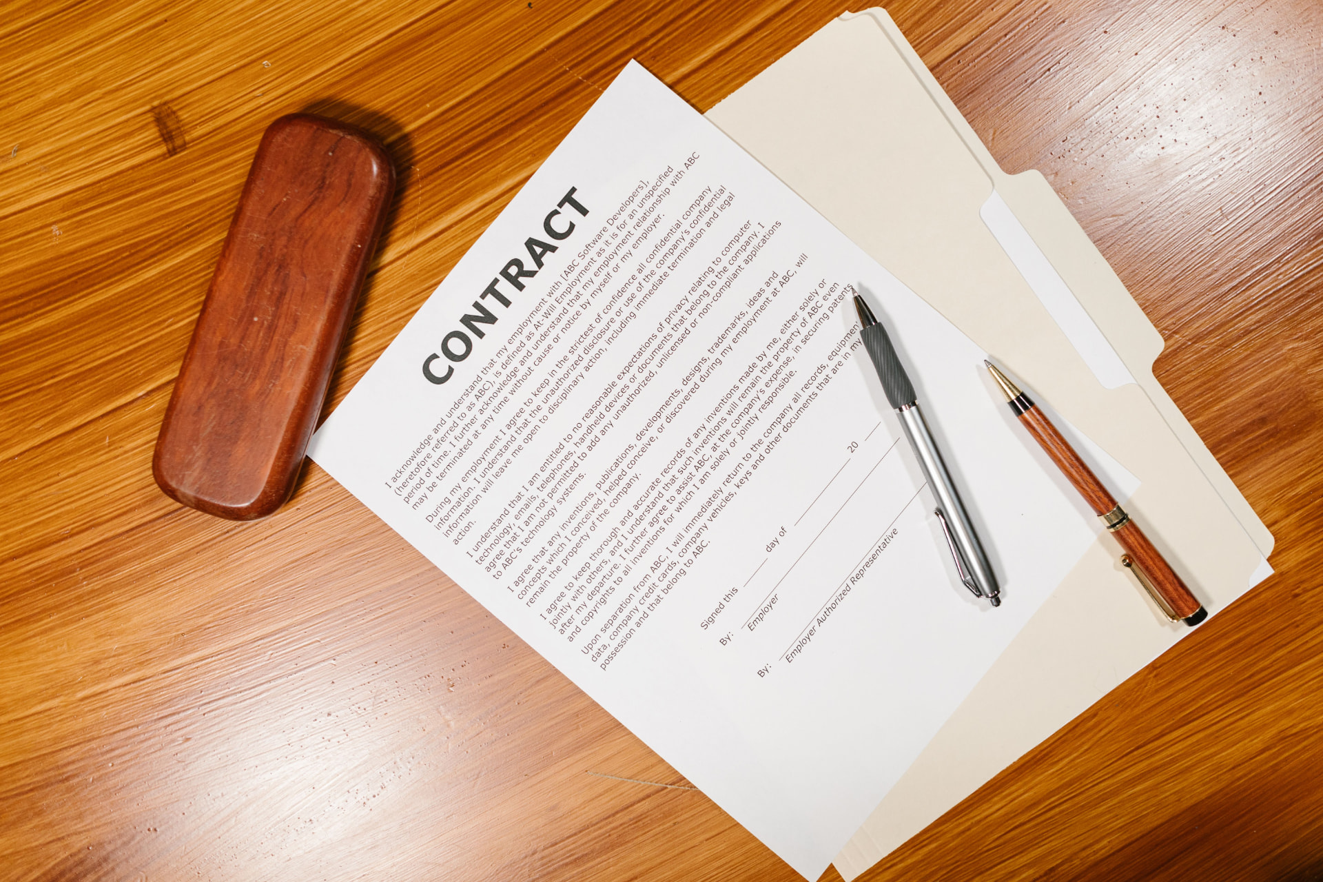 Insurance contract paperwork with pens and a file folder on a wood desk